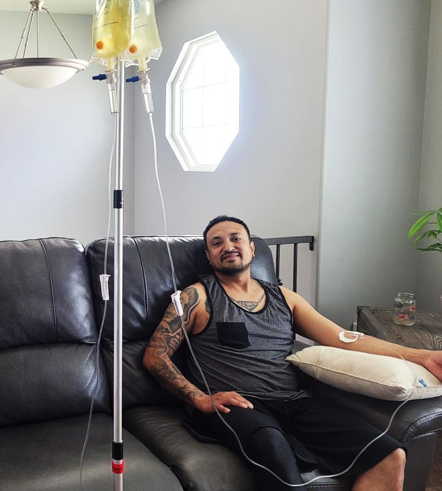 A man with tattoos comfortably receiving a mobile IV wellness drip on a leather couch.