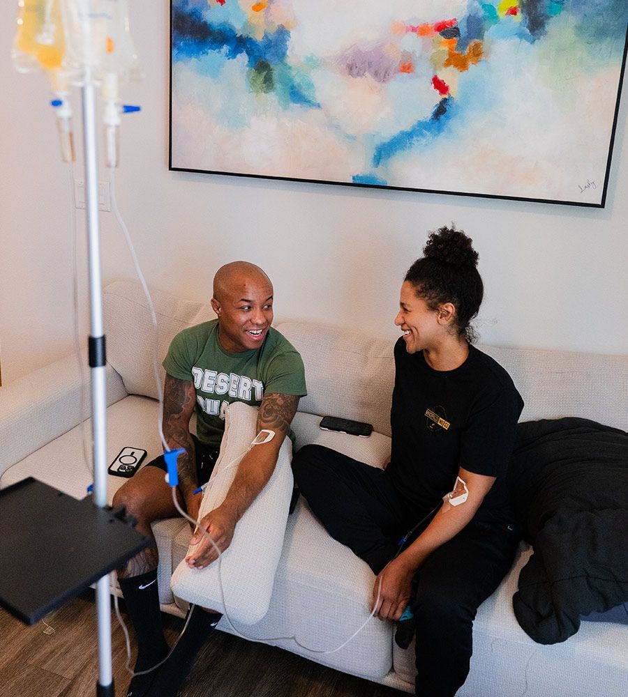 Smiling athletic couple sitting on a couch receiving simultaneous mobile IV therapy, ideal for rapid muscle recovery, performance enhancement, and hydration after intense workouts.
