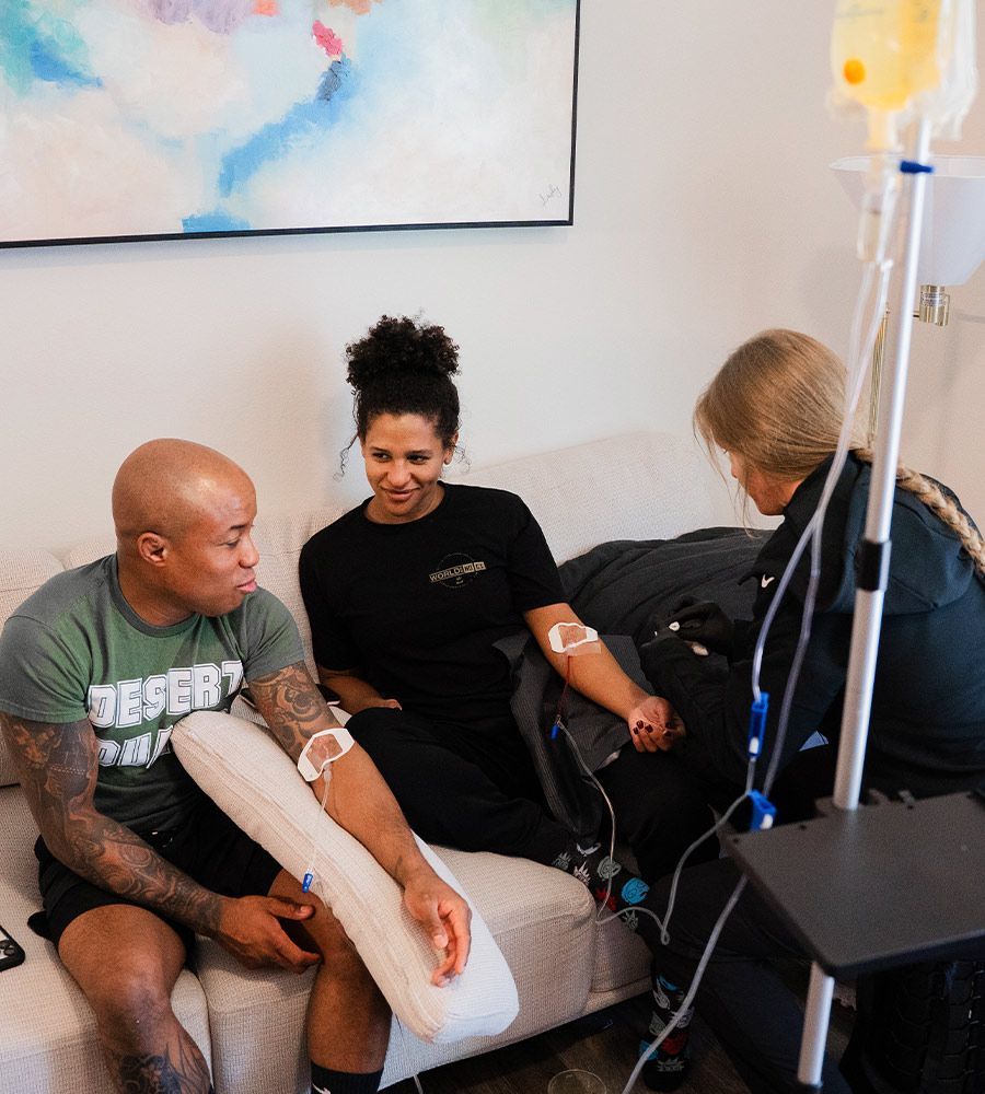 Athletic couple receiving simultaneous mobile IV therapy infusion at home from a professional nurse, ideal for rapid muscle recovery, performance, and hydration after workouts.