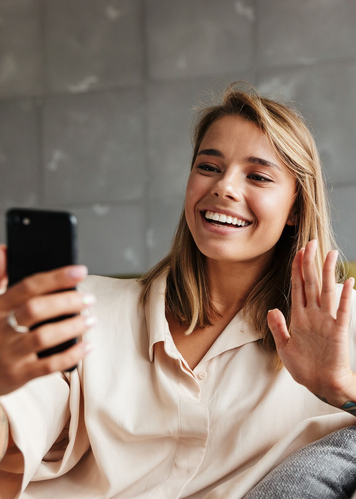 A person smiling and waving at their phone while on a video call.