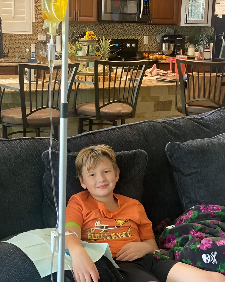 A person rests on a sofa while receiving IV therapy from a tall pole in a home setting.