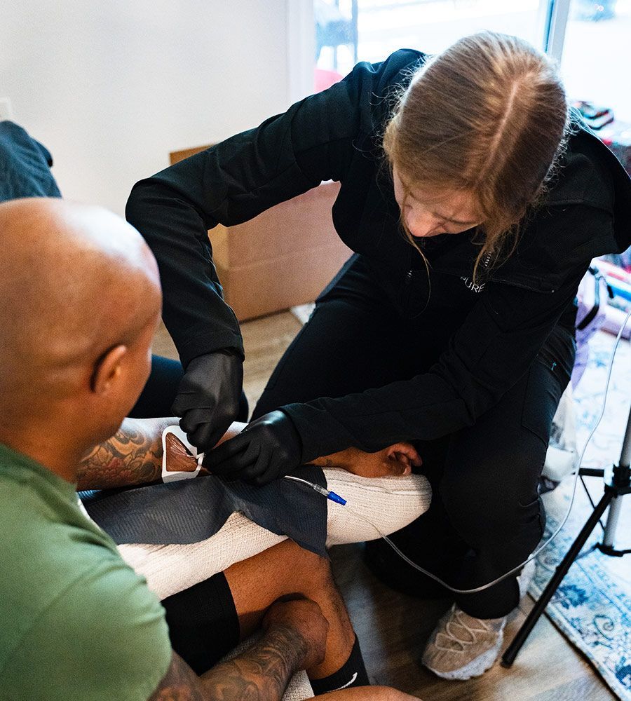 Close-up overhead view of a professional nurse in black gloves precisely starting the IV line on a male client's arm, showcasing sterile technique and personalized service for home infusions.