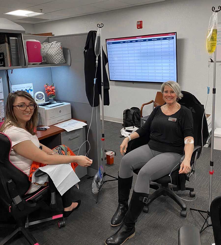 Two people receiving IV drips in an office setting. They are smiling.