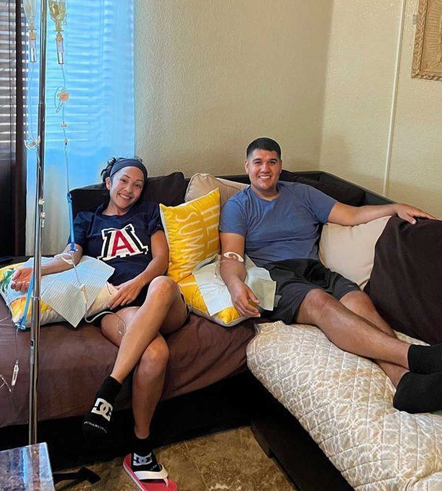 Smiling couple receiving tandem IV vitamin drip therapy together on their couch, highlighting the convenience of mobile in-home service.