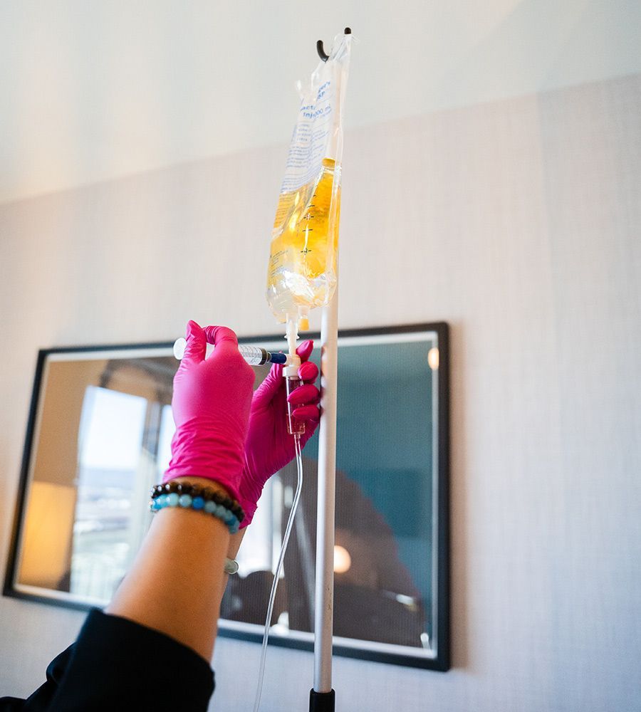 Mobile IV therapy specialist adjusting the drip and adding a customized nutrient formula from a syringe into the hydration bag.