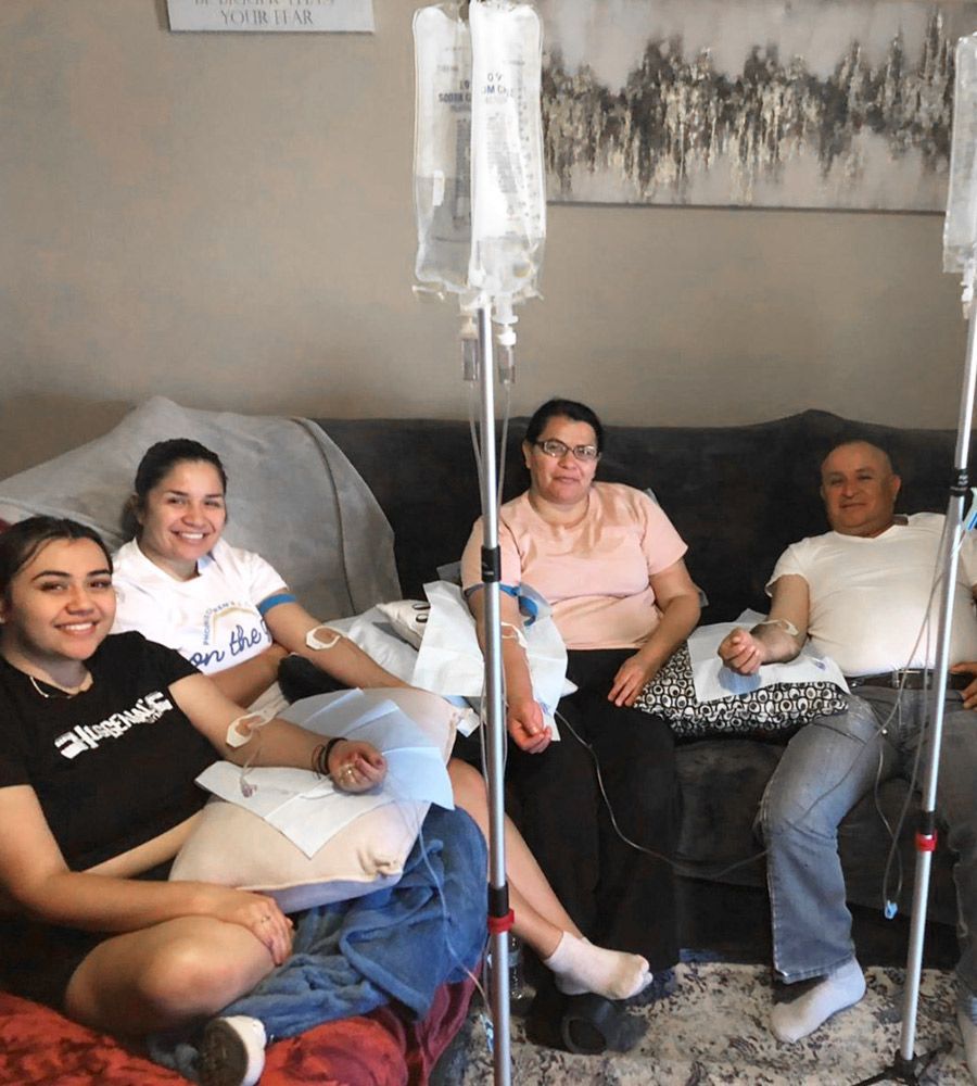 Four people on a couch receiving IVs at home. Two hang from poles. Smiling expressions.