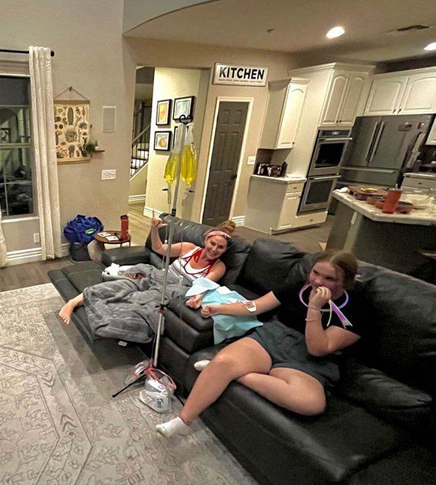 Two people relaxing on a sectional sofa near a kitchen while sharing a mobile IV therapy session.