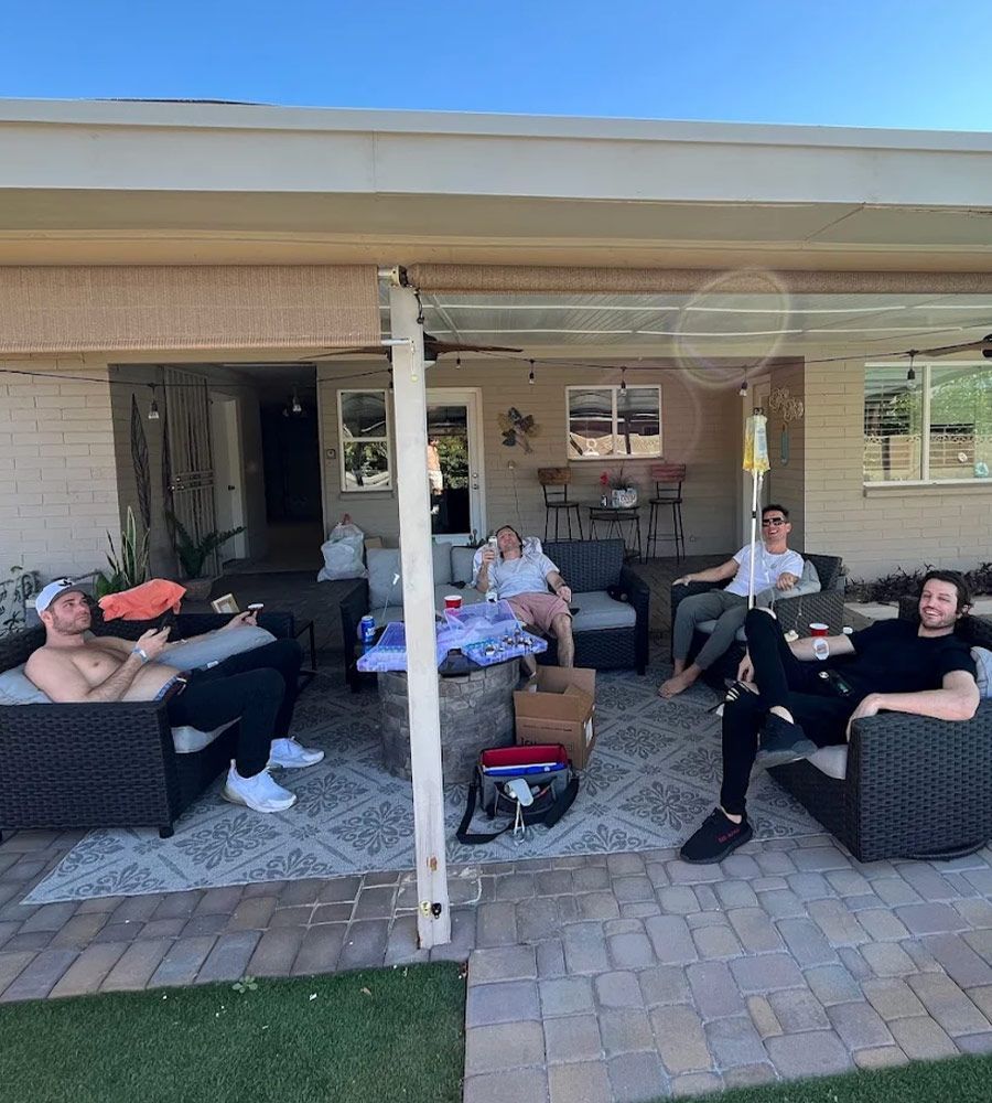 A group of friends relaxing on patio furniture during a group IV hydration session at a home gathering.
