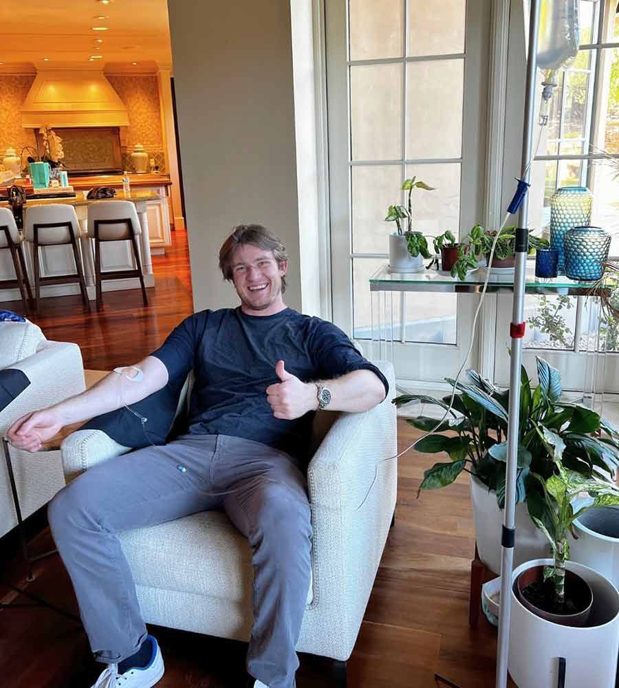Happy young man giving a thumbs up while receiving a mobile IV infusion in a comfortable chair in a modern, luxury home.