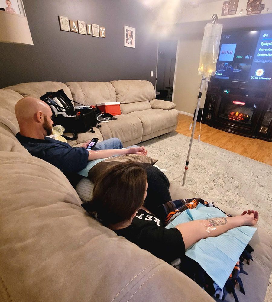 A couple receiving mobile IV treatments while watching TV together on a sectional sofa.