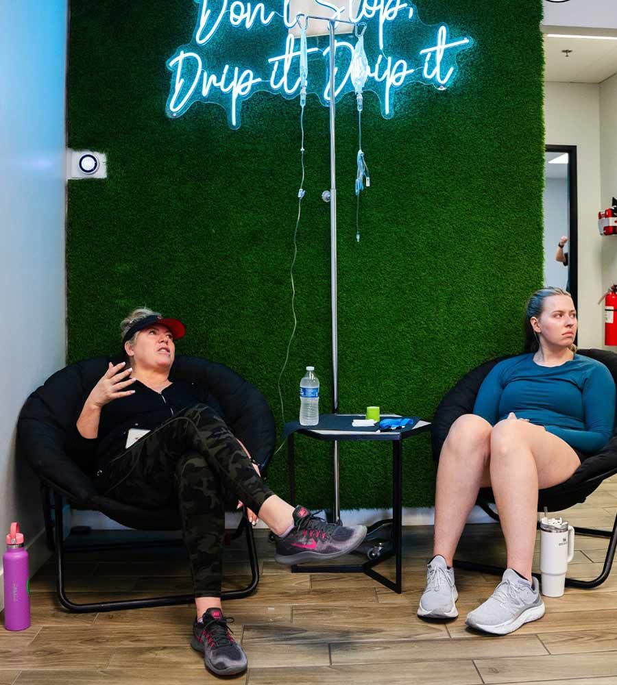 Two women in chairs under a neon sign that says