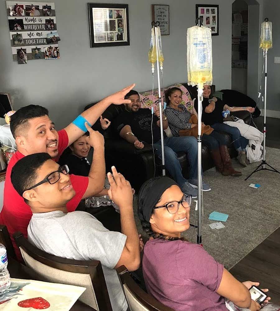 A happy group of friends or family enjoying a mobile IV hydration party session in a living room, with yellow IV bags visible.