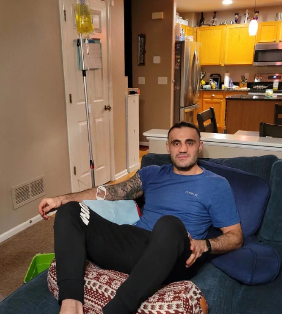 An athletic, tattooed man relaxing in a comfortable brown chair while receiving an IV infusion.