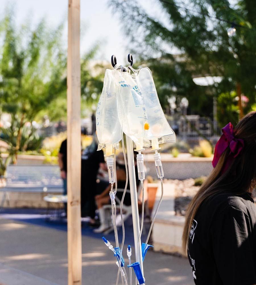 Multiple IV hydration bags hanging on a drip stand outdoors at a festival or mobile wellness station.