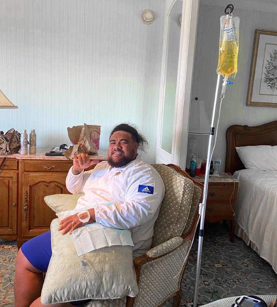 A man giving a hand gesture while receiving mobile IV hydration therapy in a home setting.