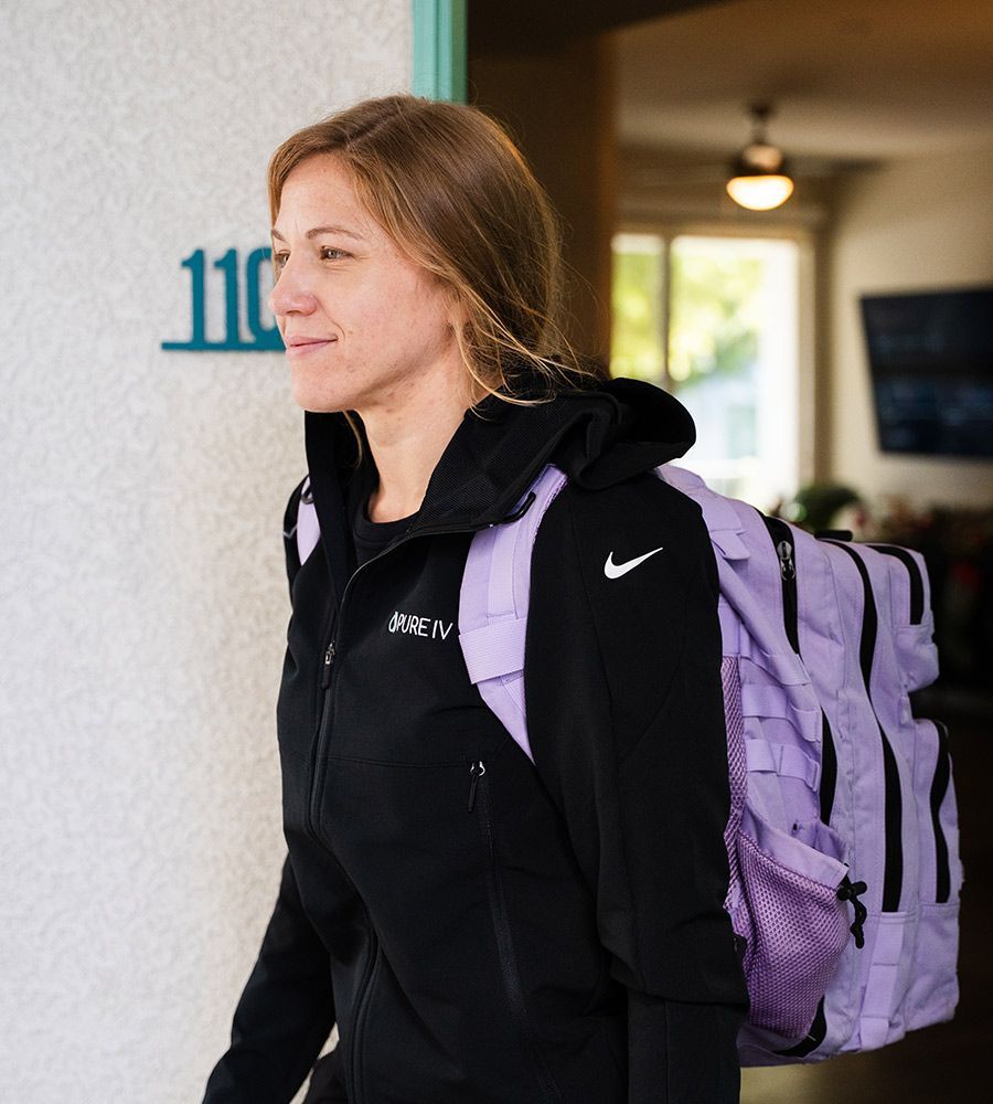 Professional PURE IV mobile nurse (Jaret) arriving at a client's location, carrying a lavender supply backpack, emphasizing the convenient on-demand and fully equipped nature of the in-home IV hydration service.