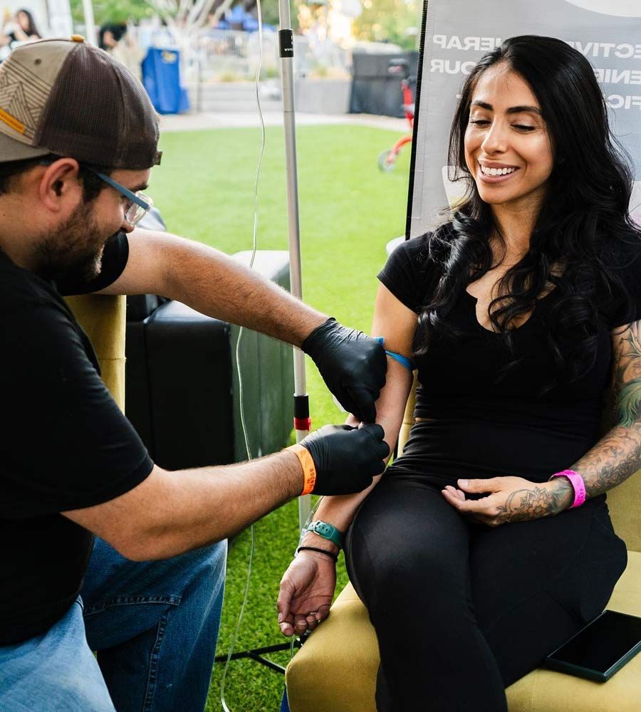 Man giving woman an IV infusion outdoors; both smiling.
