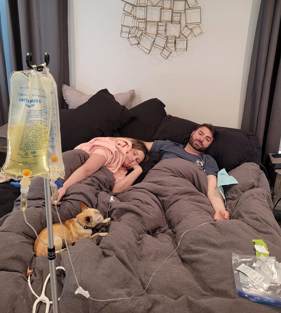 A couple and their small dog resting in bed while receiving mobile IV hydration therapy.
