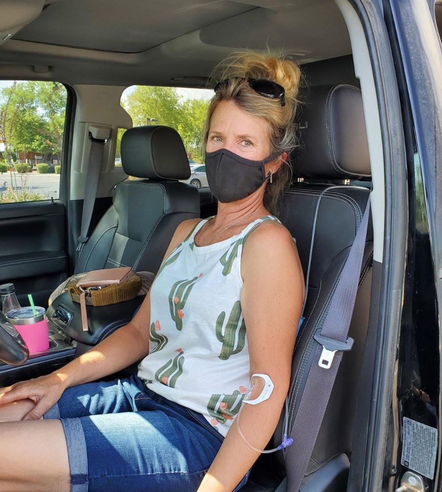 Woman in car with medical tubing, wearing cactus tank top and mask.