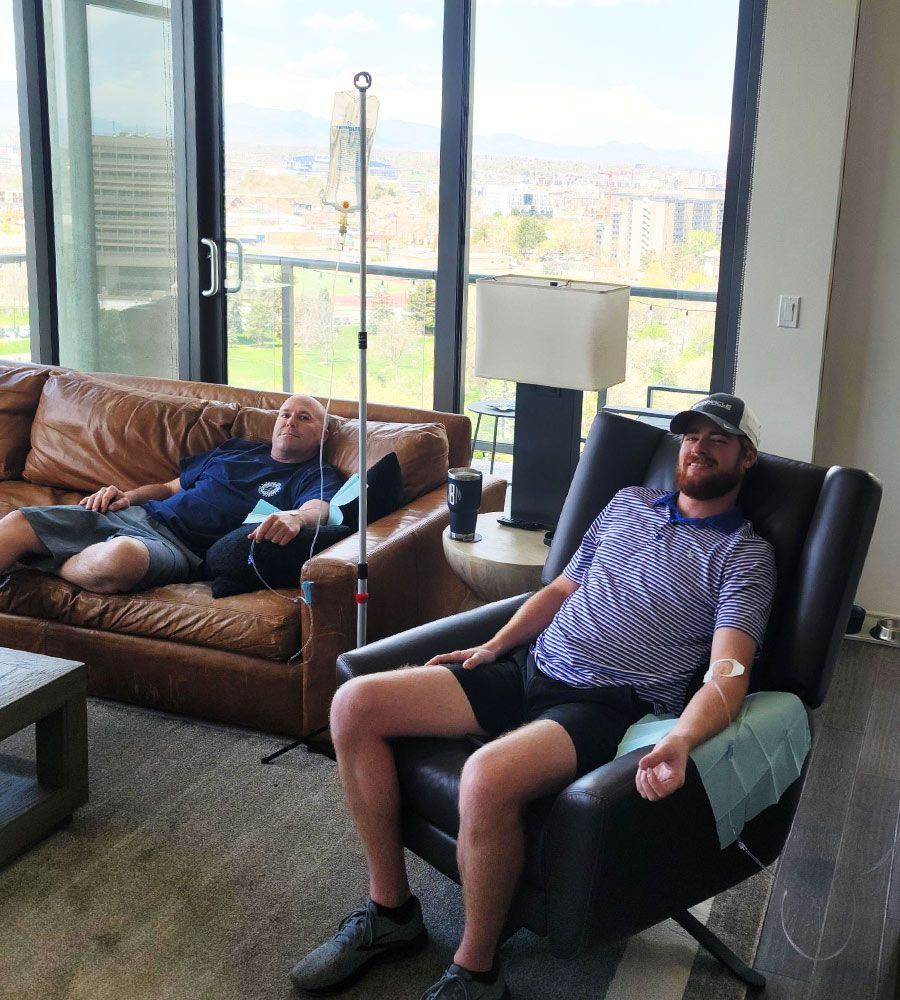 Two men receiving IV hydration therapy in a modern apartment with a scenic city view.