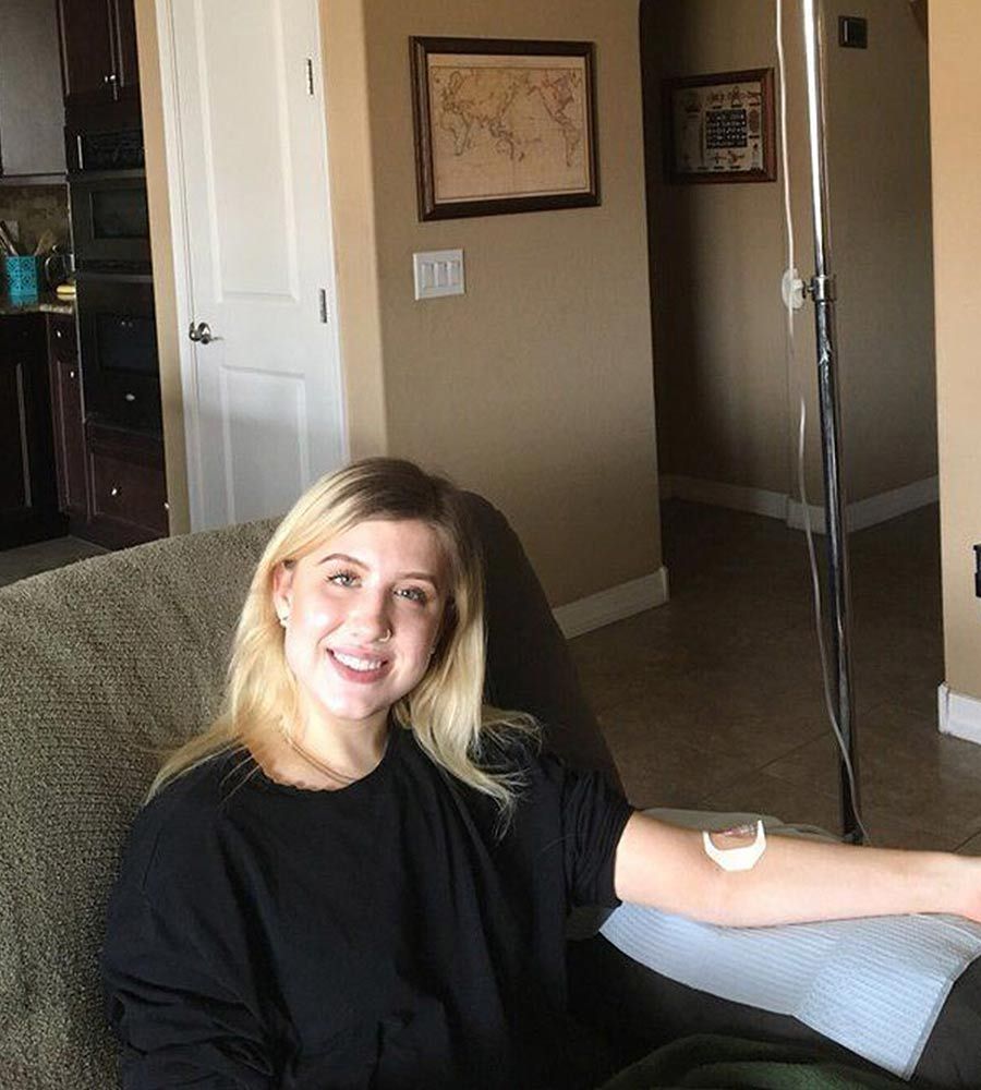 Smiling young woman receiving a mobile IV vitamin infusion treatment comfortably on her couch in a warm, inviting home setting.