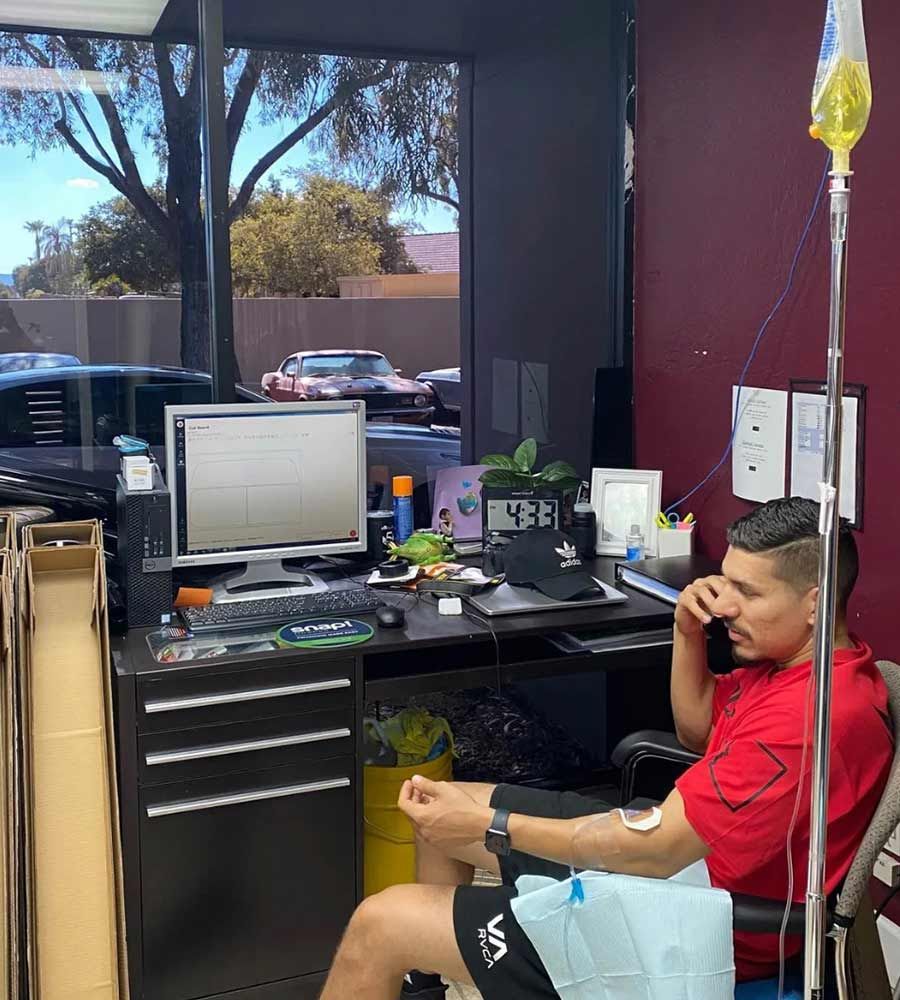 Man talking on the phone at his computer desk, receiving mobile IV hydration therapy, promoting business wellness and maximizing productivity during the workday.