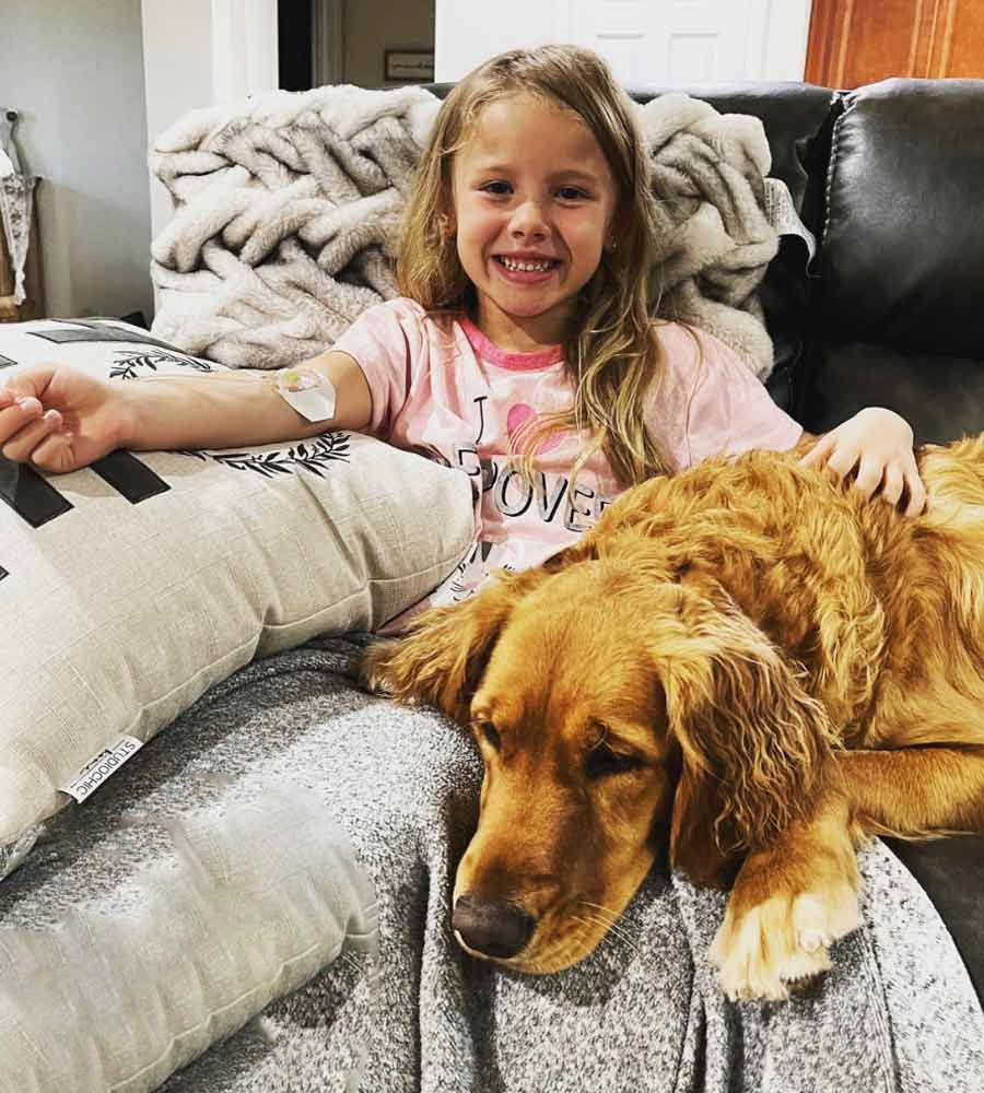 A licensed nurse providing pediatric at-home IV therapy while a family dog sits nearby.