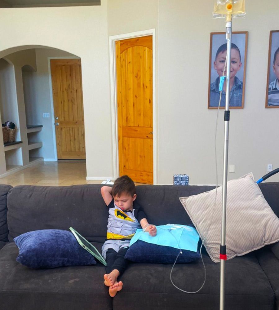 A young boy in a Batman shirt resting on a couch during an at-home IV hydration treatment.