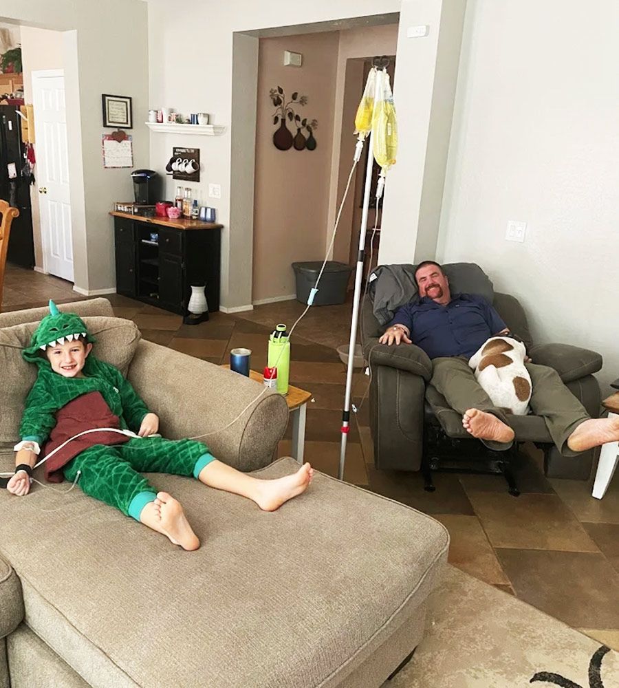 A young boy in a dinosaur costume and an adult receiving at-home IV therapy together.