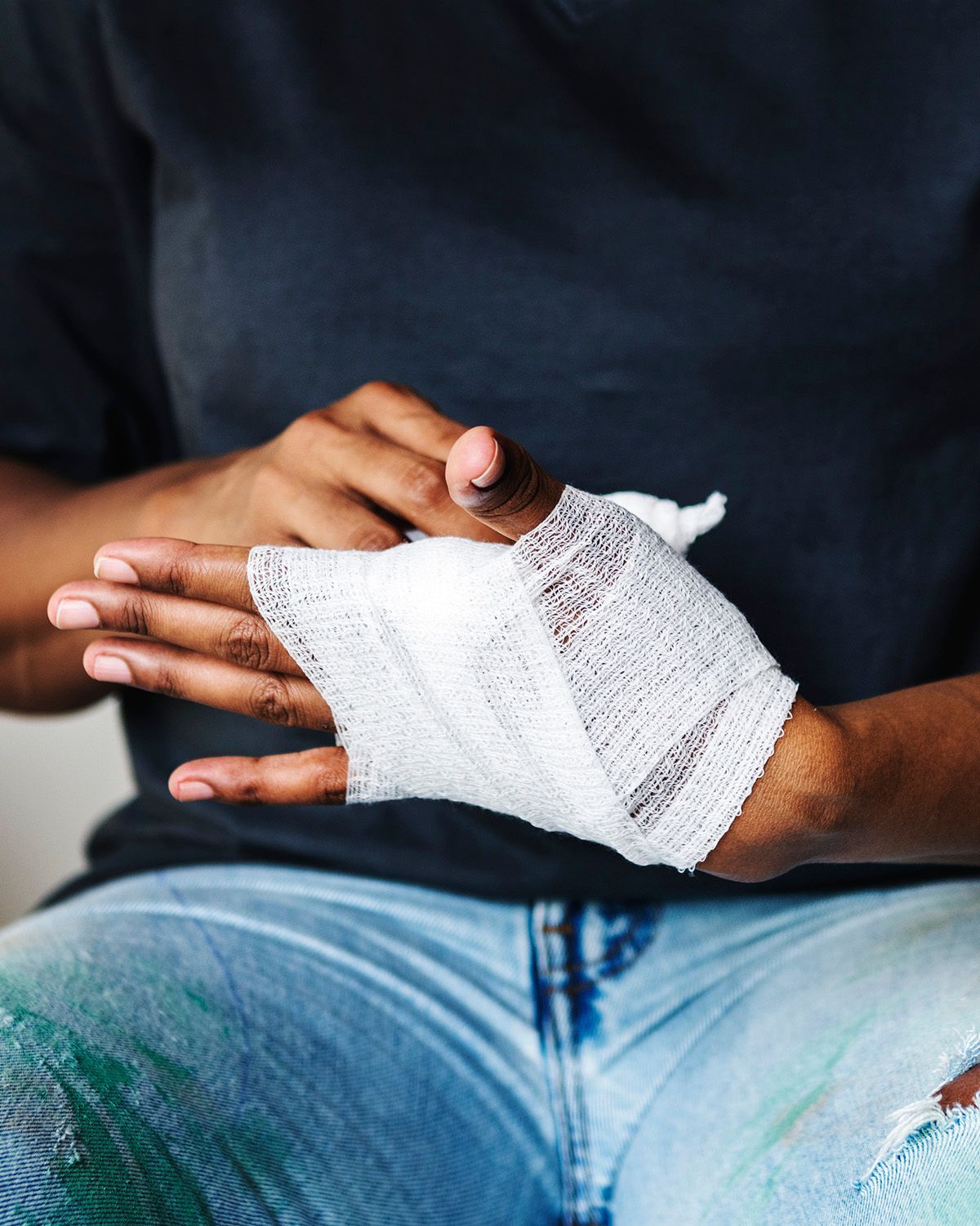 A person wraps a white medical gauze bandage around their hand.