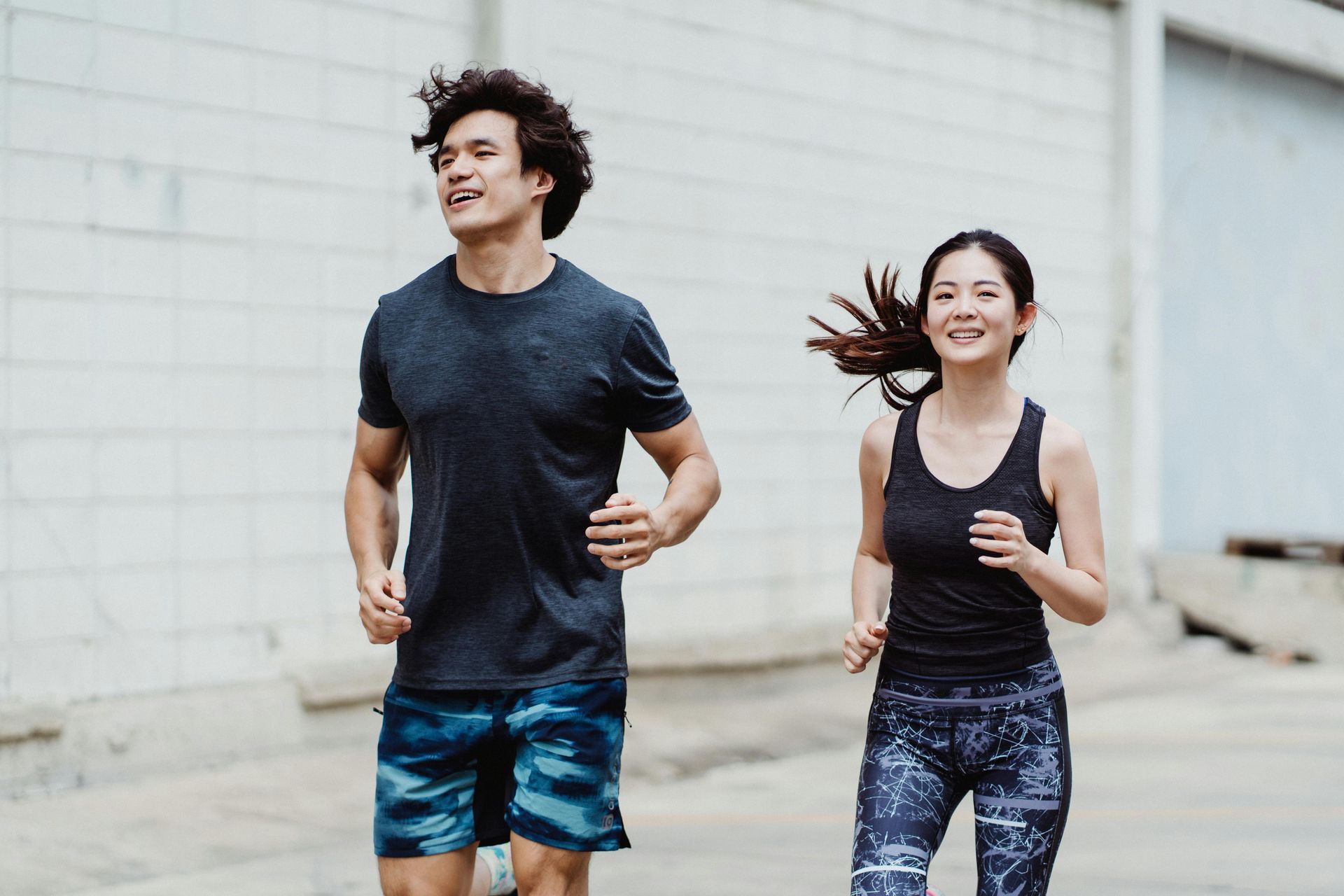 Man and woman running outdoors, smiling. They wear workout clothes.