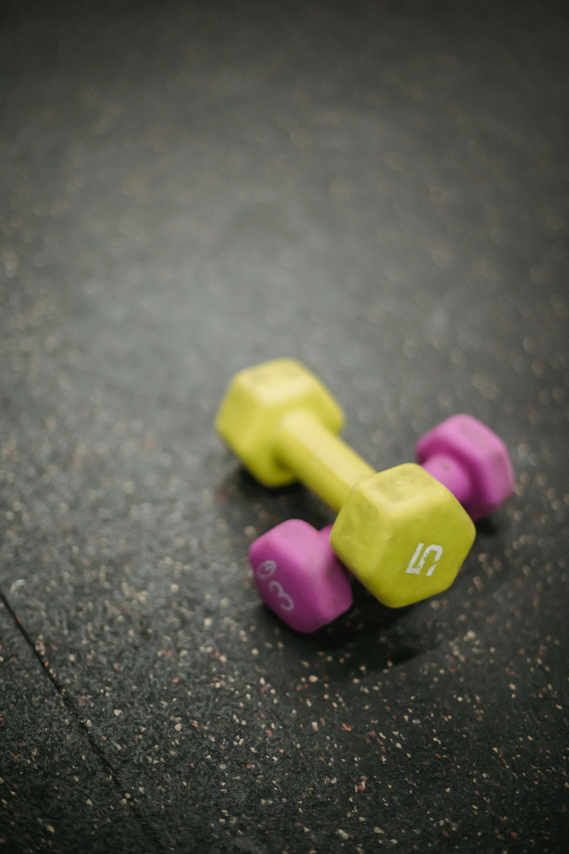 Yellow and purple 5-pound dumbbell on a dark textured surface.