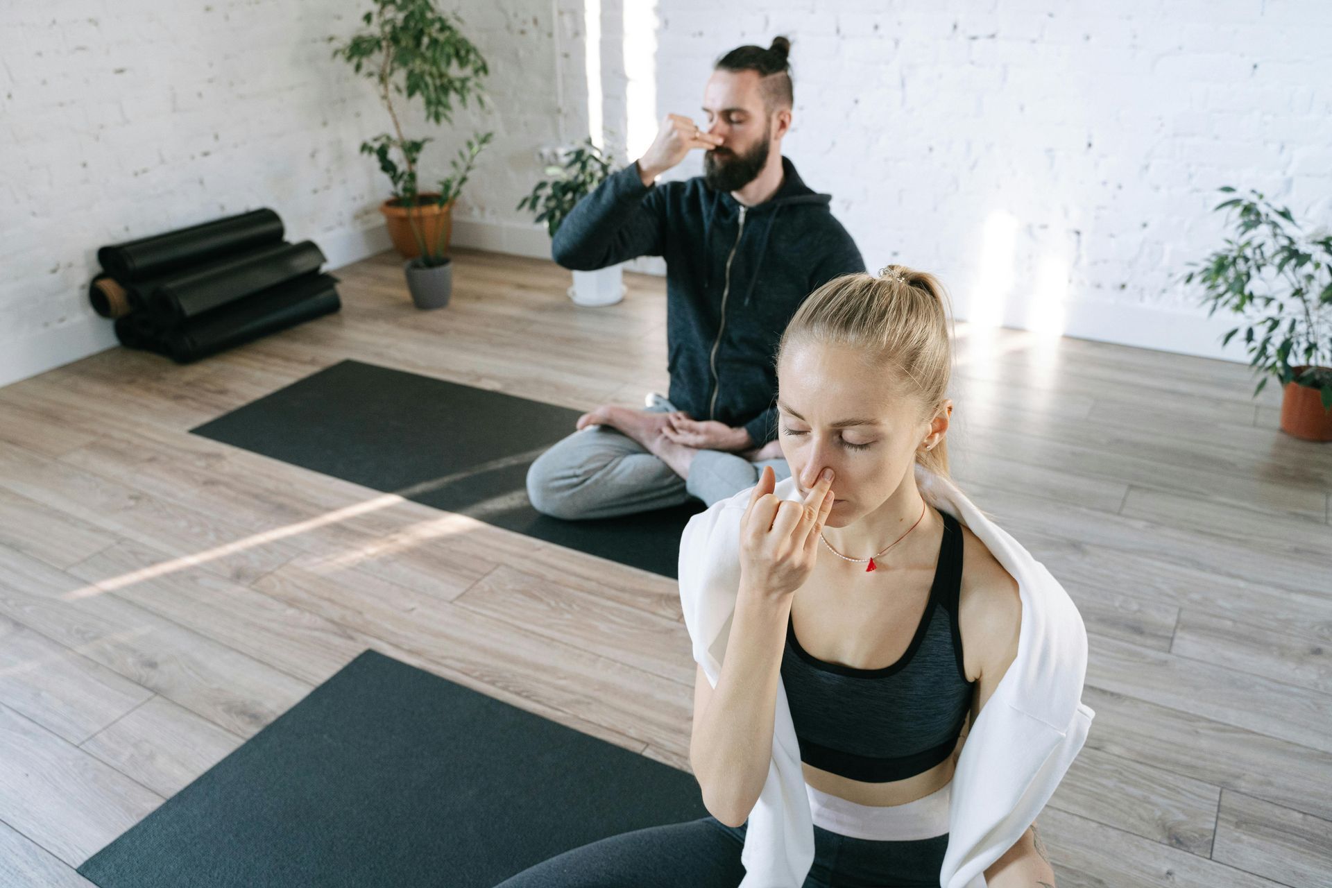Woman and man practicing alternate nostril breathing in a bright studio, on mats.
