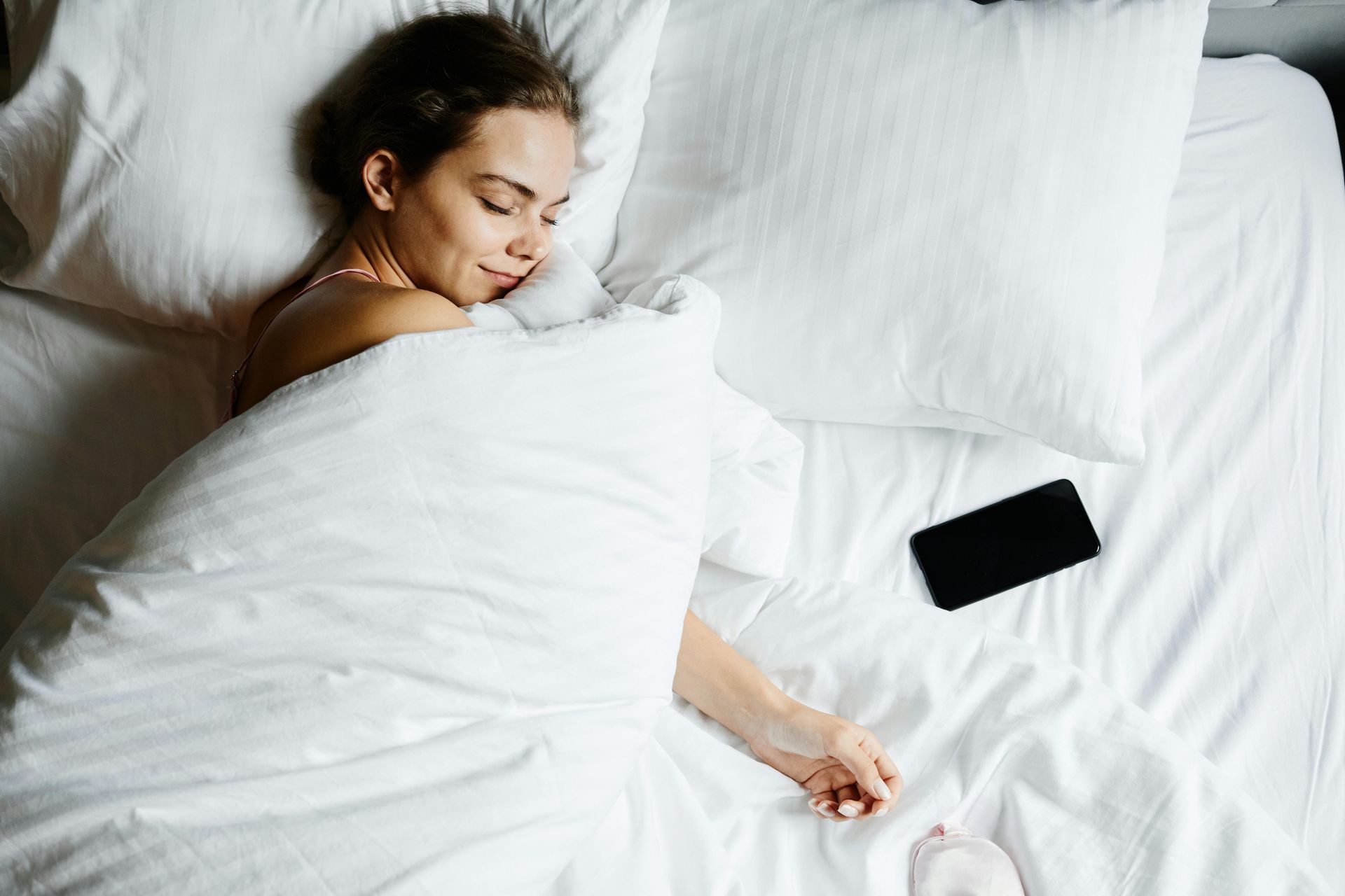 Woman sleeping in white bed, with phone.