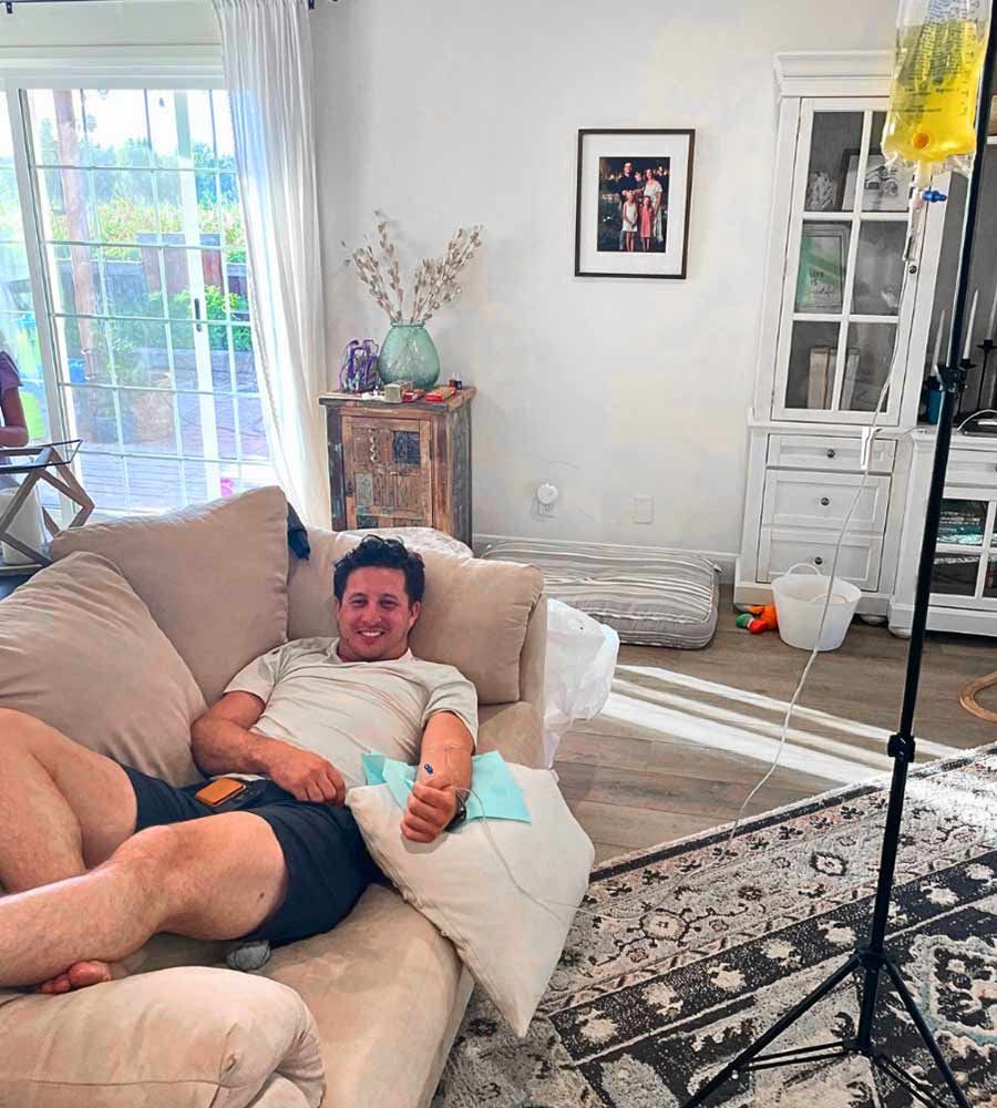 Man on a sofa with a thumbs-up receiving a relaxing in-home IV drip treatment.