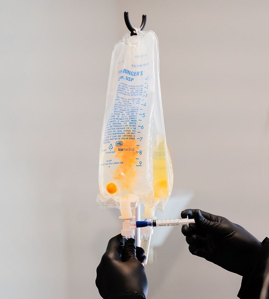 Ringer's Solution IV bag receiving added nutrients via a syringe, demonstrating the preparation process for mobile hydration and wellness treatments.