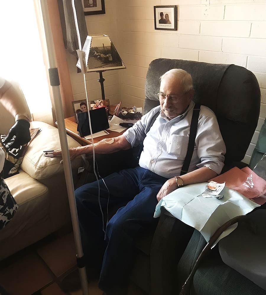 Senior patient getting IV therapy administered by a caregiver in a comfortable living room setting.
