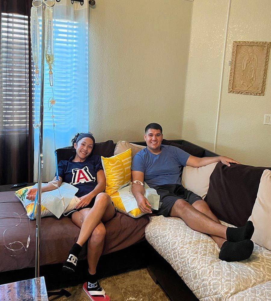 Smiling couple sitting on a couch receiving simultaneous in-home IV hydration therapy treatments.