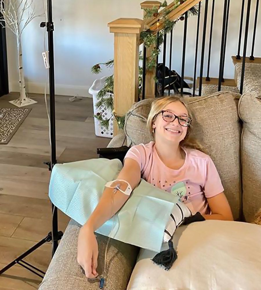 A smiling girl wearing glasses comfortably receiving a mobile IV wellness treatment at home.