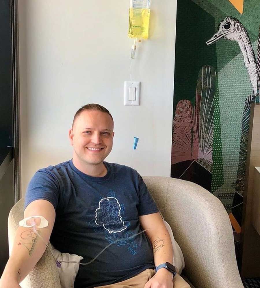 Man receiving IV infusion, smiling in chair, with a yellow bag hanging.