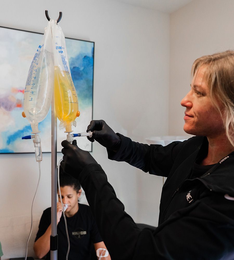 Professional PURE IV nurse in black gloves injecting customized vitamins or medications from a syringe into an IV hydration bag, ensuring sterile preparation for the client's personalized mobile infusion treatment.