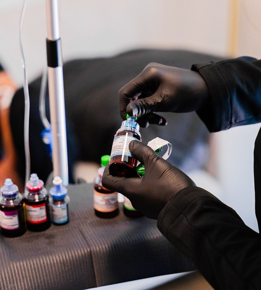 Close-up of professional's black-gloved hands carefully preparing a vial of concentrated vitamins for mixing, emphasizing sterile technique and high-quality, customized ingredients for IV infusion.
