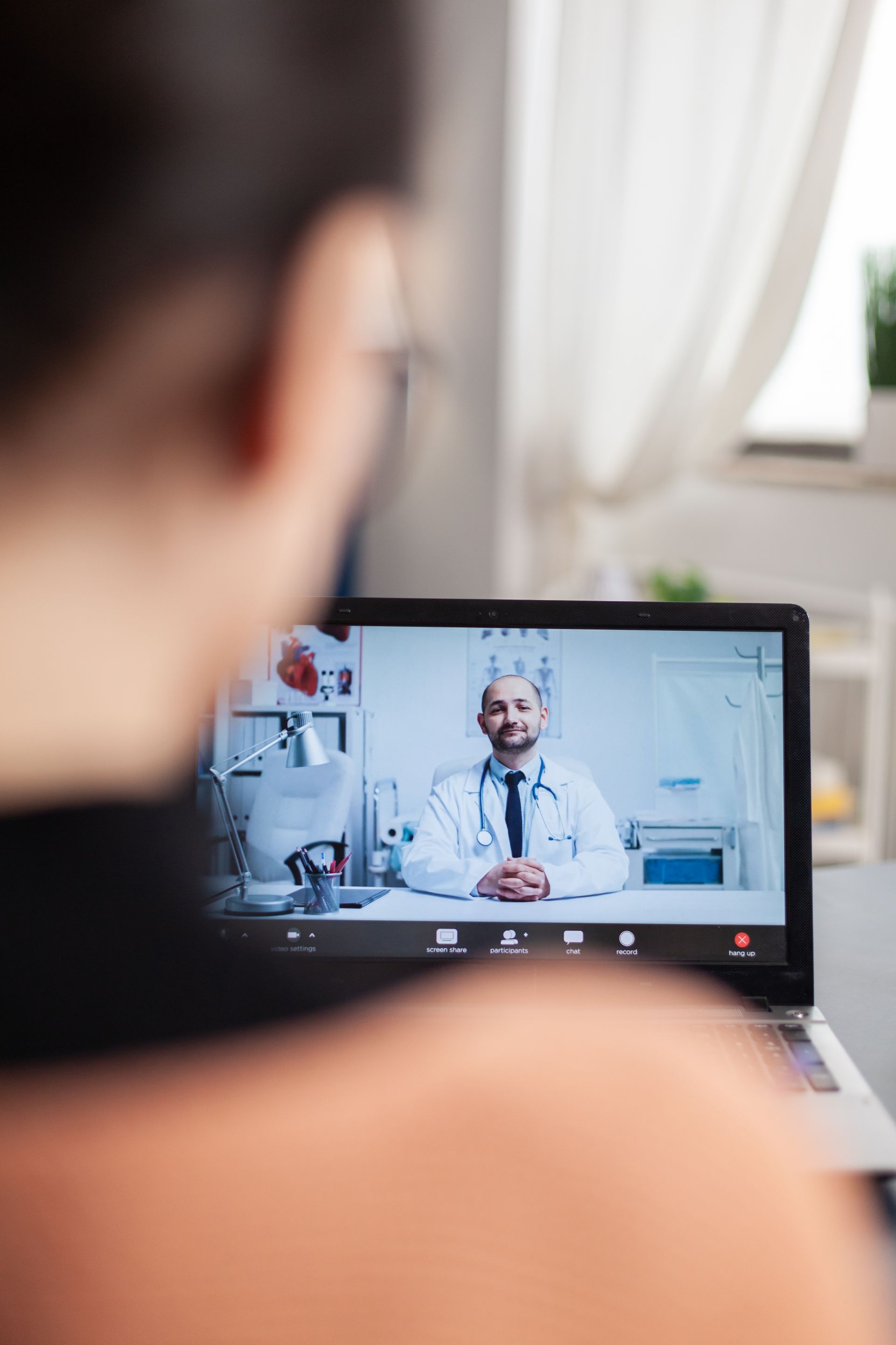 An individual participates in a remote medical consultation via video call on a laptop.