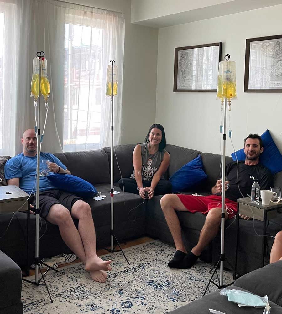 Three friends comfortably relaxing on a sectional couch while receiving mobile IV hydration drip infusions in a modern living room.