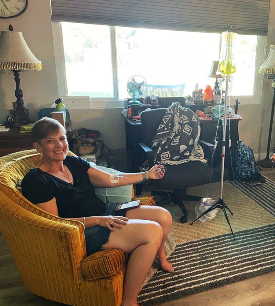 A smiling woman sitting in a yellow armchair at home receiving a mobile IV infusion.