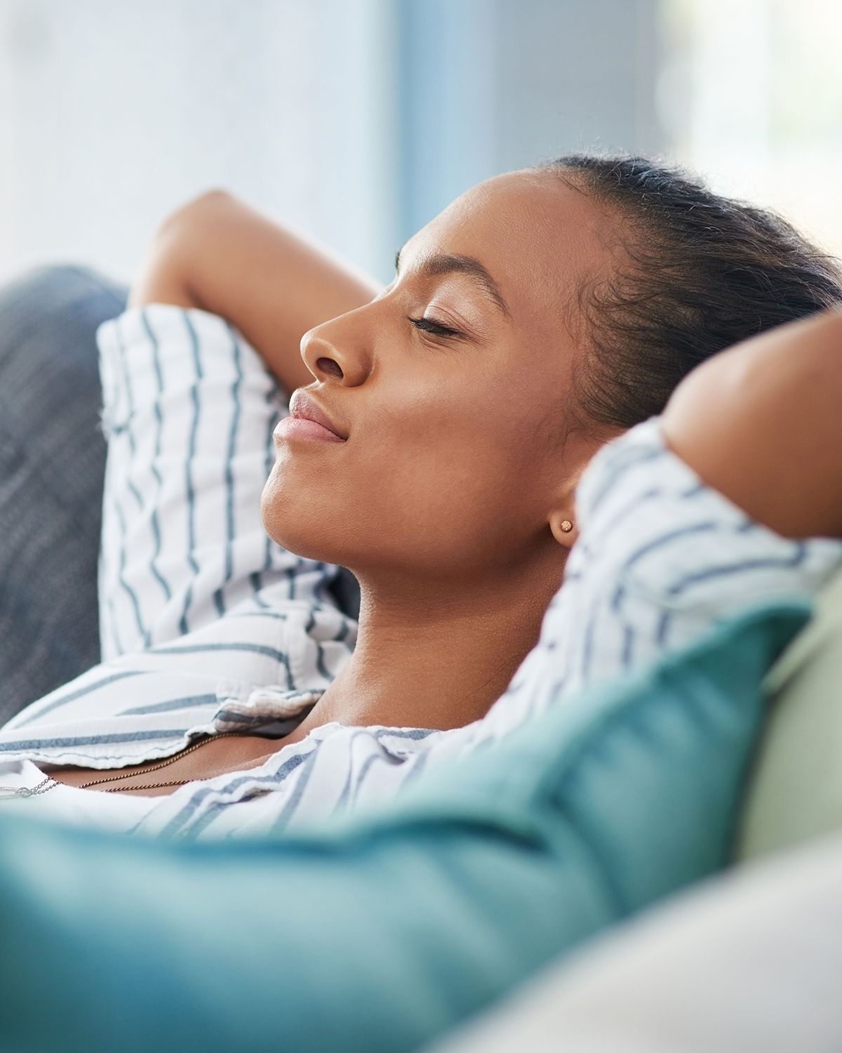 A person reclining on a couch with hands behind their head, eyes closed and appearing relaxed.