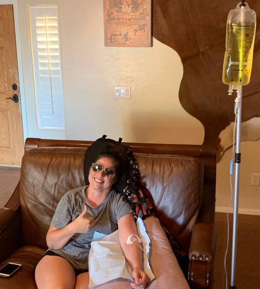 Office worker with a headband smiling while receiving an intravenous infusion in a functional, professional setting.