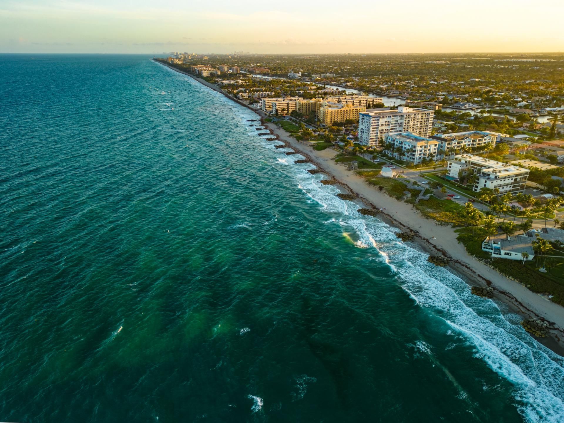 Aerial view of a coastline with turquoise water, sandy beach, and buildings in a town.