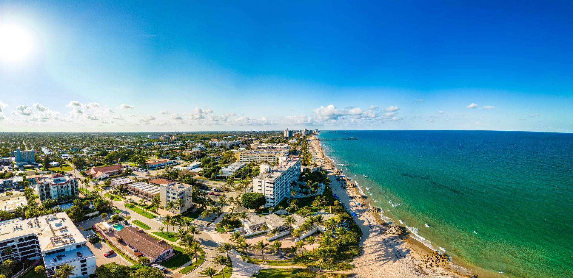 Aerial view of a beach town with clear blue sky, turquoise water, and buildings along the coast.