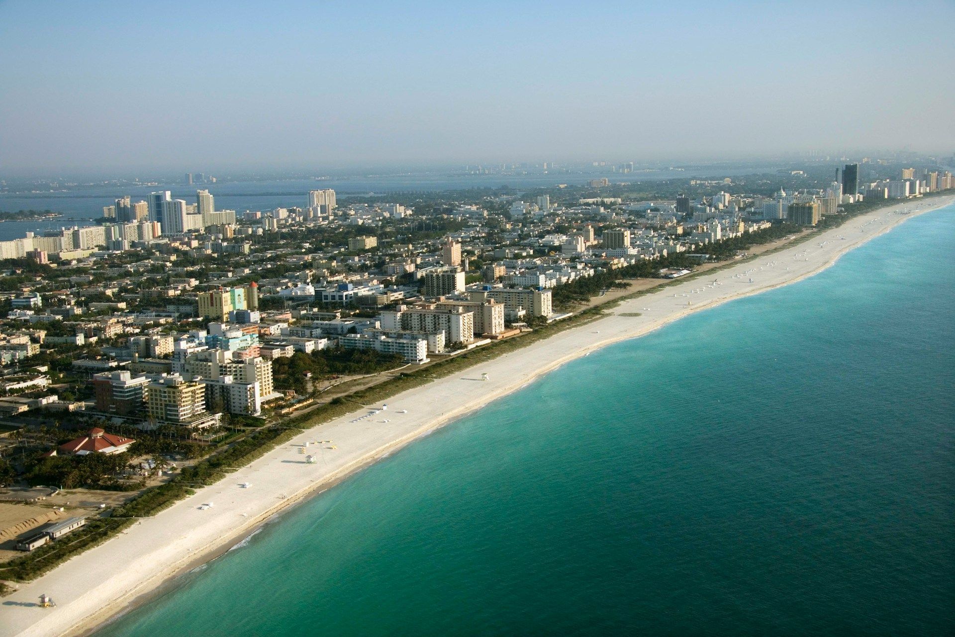 Aerial view of a coastal city with a long white sandy beach and turquoise water under a clear sky.